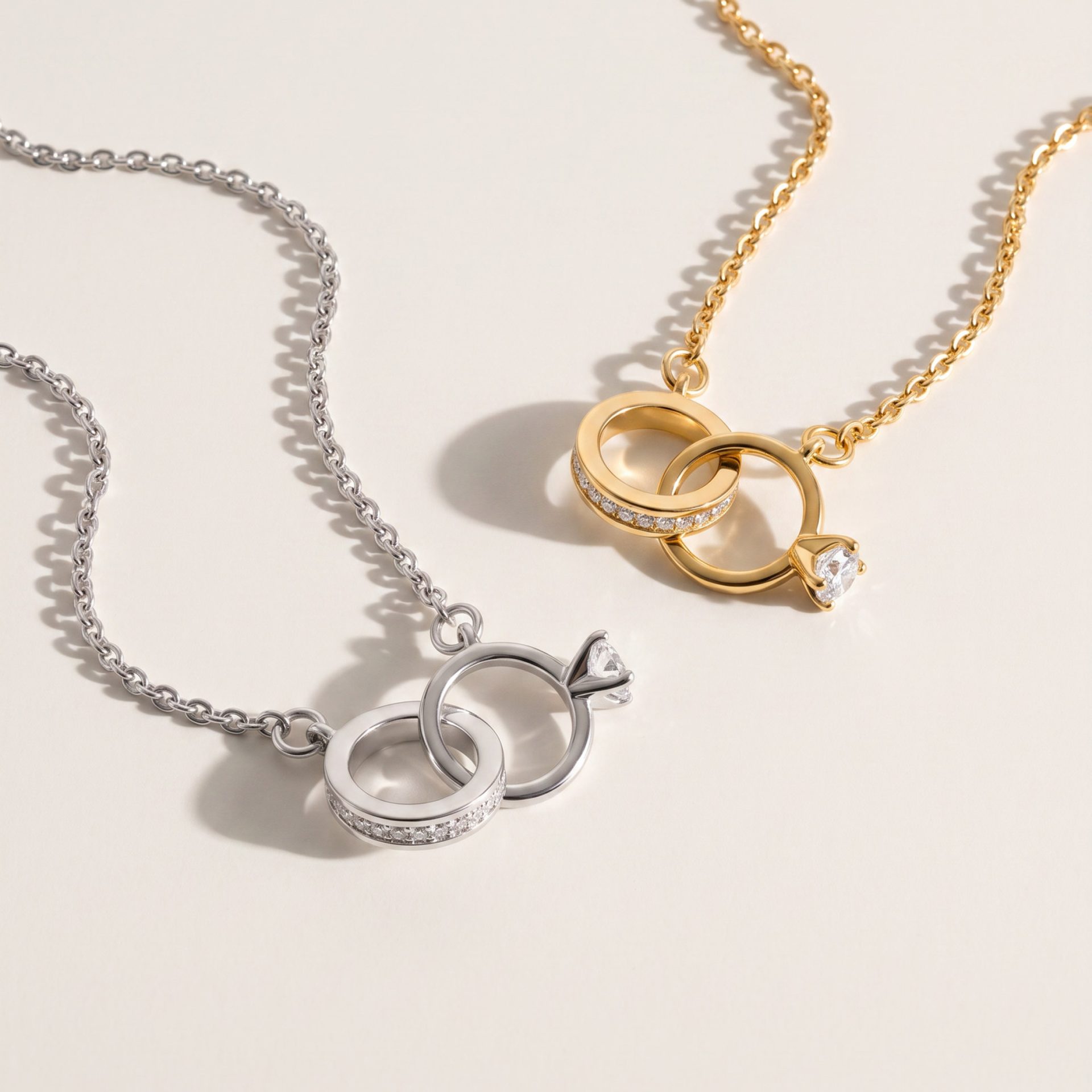 Gold and silver necklace chains with interlocking rings and embedded diamonds on a pale background, jewelry display still life.