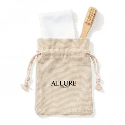 Beige fabric drawstring pouch with 'ALLURE Jewellery' logo, containing a white card and a wooden toothbrush against a white background.