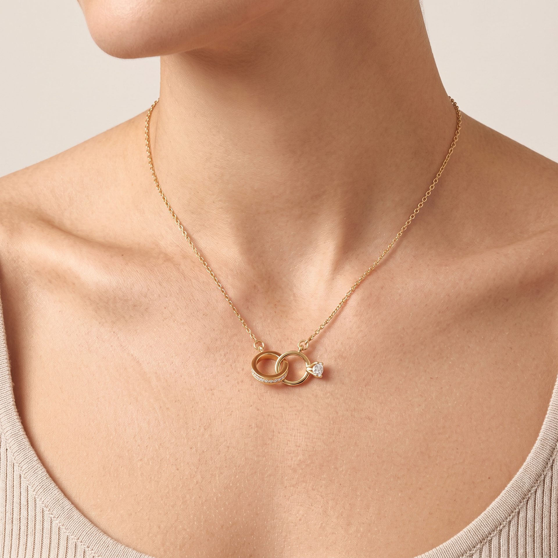 Gold chain necklace with interlocking rings pendant resting on a woman's collarbone against a beige knit top.